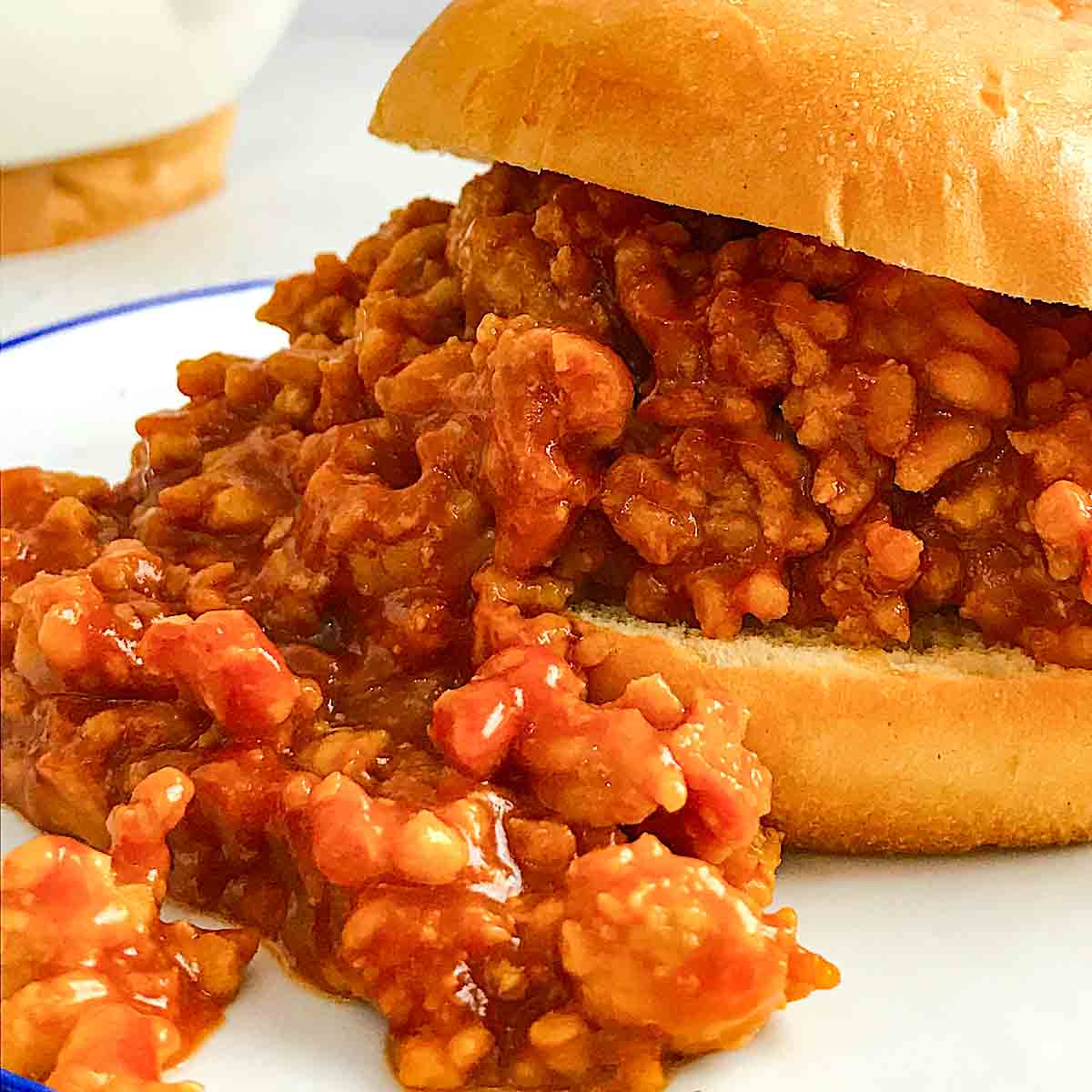 Close shot of a burger bun with some cooked ground meat on it on a while plate with 